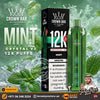 Crown Bar Alfakher Mint Crystal V2 disposable vape and its packaging box, set against a green mint leaf and ice splash background. The ad includes branding, product details, and a store contact banner.